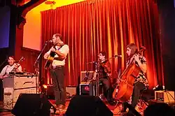 A color photograph of a four-person band performing on stage.