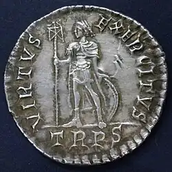 Silver coin showing a man standing with a standard and a round shield behind his legs. There is writing round the edge including "TRPR" below the figure.