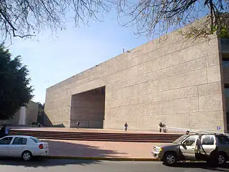 A street-level photo of the windowless side of the stone headquarters building, with a small plaza and several stairs leading down to sidewalk level in the foreground at Barranca del Muerto 280, Guadalupe Inn, Álvaro Obregón, 01020 Ciudad de México, CDMX, Mexico