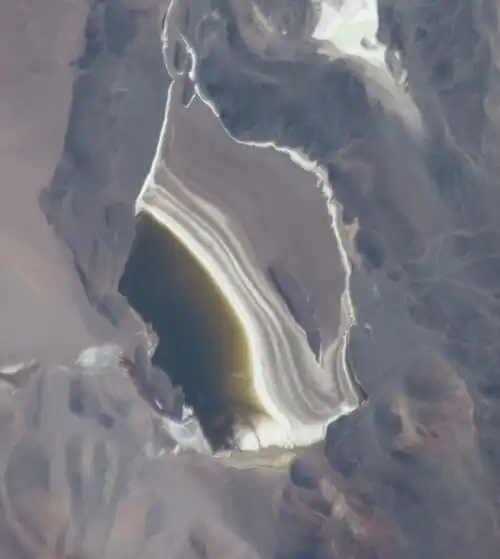 High-elevation photo of a brown lake with a white-brownish plain next to it
