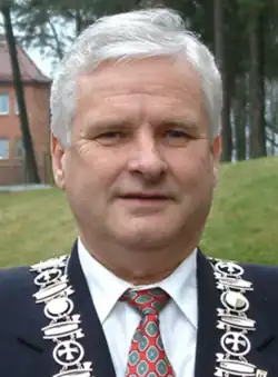 A grey-haired caucasian male in his fifties wearing a suit and official regalia