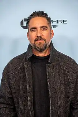 Jimmy LaValle wearing a black sweater and a dark gray coat, smiling and looking straight at camera