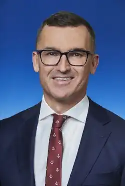 Man with glasses speaking at a microphone