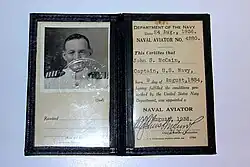 Color photograph of a framed document, on the left page is a black and white photograph and on the right page is a certificate