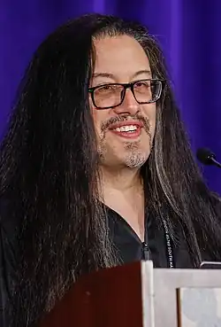 Portrait photo of a Hispanic man with dark long thick hair and glasses at a podium