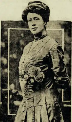 B&W portrait photo of a standing woman wearing a hat and a pale-colored suit.
