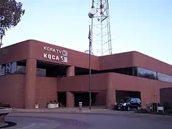 A two-story, brick-building with a large transmission tower behind it and KCRA and KQCA signage