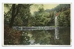 A calm lake with refelctions in the water, to the right is Stone Tower studio behind trees