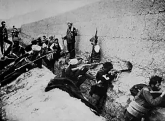 Men with guns crouching in a trench and leaning against a defensive wall