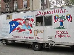 A trailer painted with the title "Aguadilla" and "Cocinando con Salsa Sason y Sabor" and decorated with paintings of a Puerto Rican flag, drums, and a frog