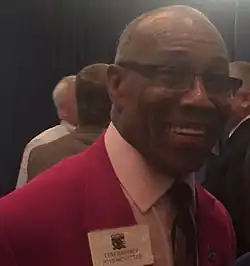 Lem Barney smiling in a red suit jacket, shown from about the shoulders up.