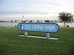 A blue sign stands in the middle of a park. "Leo J. Ryan Park" is written on it.