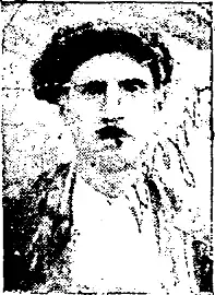 Grainy picture of a young man with a short moustache and a working-class Greek outfit, including a flat cap