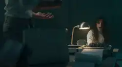 Cabello is strapped to a polygraph while wearing a white straitjacket on the viewer's right. To the viewer's left is a person confronting her with their palms facing up.