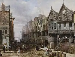 A street in the 19th century with buildings on the left, the first of which is timber-framed and highly decorated. In front of the house is a horse and cart