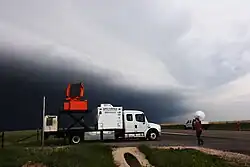 Two white trucks scanning a storm with instruments on their backs. The UMass X-POL is visible to the right, mounted on the bed of a truck.