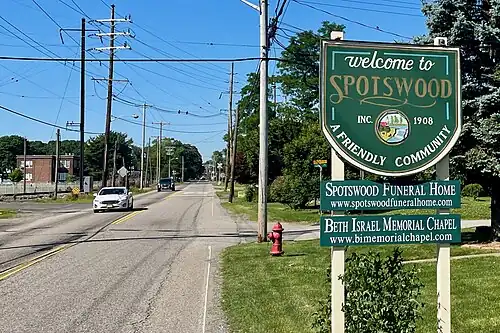 Suburban road with trees; there's a welcome sign in the foreground