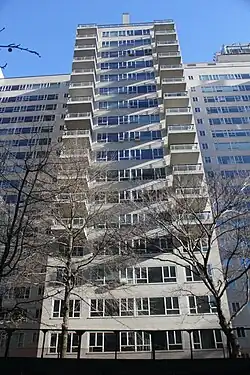 One of Manhattan House's wings as seen from ground level. The wing protrudes from the main portion of the building. The facade is made of white brick, with glass windows, and there are balconies on several stories.