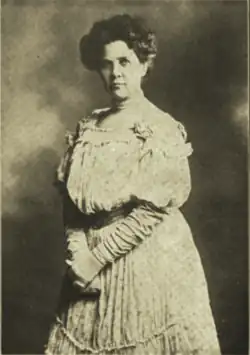 B&W portrait photo of a middle-aged woman with her hair in an updo, wearing a pale-colored dress and gloves.