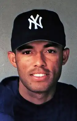 A man in a black baseball uniform and a baseball cap with an interlocked white "NY" on the front.