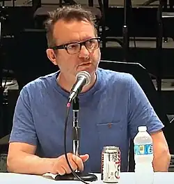 Middle-aged man with glasses and a blue shirt speaking into a microphone