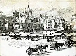 Tall narrow buildings behind an open space filled with small stalls.