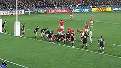 The All Blacks lined up along their try-line, with a ruck formed several metres (yards) from the try-line. Several Tongan players are positions in or around the ruck waiting for the ball to emerge.
