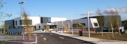 Sports centre building, with white and black cladding, set in large car park with landscaping