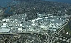 This is an image of Midway District, San Diego that was taken from a low-flying airplane facing approximately southwest. The bordering neighborhoods have been dimmed to distinguish the district boundaries. At the center is the Midway district, part of Old Town is visible at the bottom. In the background at the top left of the image is Liberty Station, and at the top center is Loma Portal.