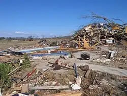 The image shows a home swept off its foundation in Alabama. A wrangled mess of debris can be seen in the background, with scattered pieces on top of the foundation. The damage would be rated EF4.