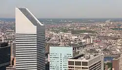 The slanted top of 601 Lexington Avenue, in the left foreground, as seen from Rockefeller Center. Other nearby skyscrapers are visible in the right foreground, while the borough of Queens is visible in the distance.