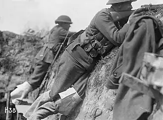 A black and white photograph of two men in military uniform pointing rifles over the lip of the trench in which they are standing