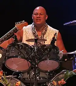 A man sits on a drum set and plays the drums at a live concert