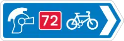 A blue direction sign with a right-pointing arrow. Three symbols (ranged left to right) are; a Roman soldier's helmet, the number 72 written in white on a red background, and a bicycle symbol.