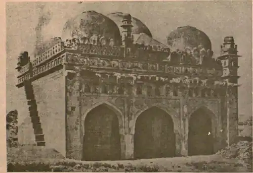 Black-and-white image of a mosque with the arched entrances on the facade. Numerous domes and pyramid-shaped vaults can be seen surmounting the mosque