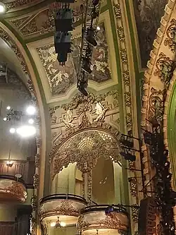 A side view of the box seats on the auditorium's left wall, looking up from the orchestra level. The two boxes are staggered; the box on the right (closer to the stage) is lower than the one on the left (farther from the stage). There are murals on the walls above the boxes.
