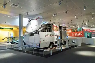 A large trailer truck with a satellite dish mounted on its rear and CONUS logo on its side inside a museum.