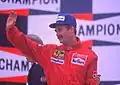 Nigel Mansell wearing a black baseball cap and racing outfits on a podium