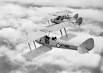 Rear three-quarter view of three biplanes in flight above clouds