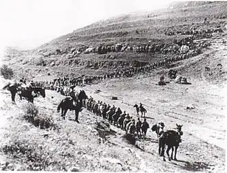 Column of soldiers marching up a hillside with mounted guards
