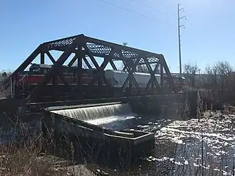 A short freight train crossing a truss bridge over a small dam