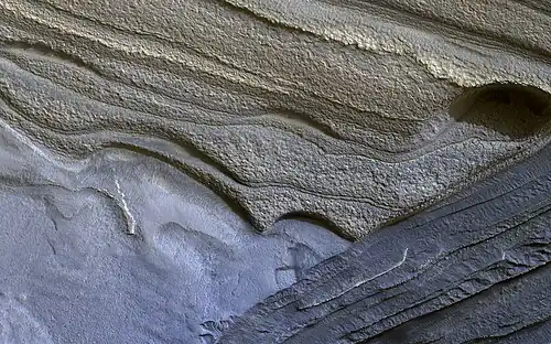 Image 11 Climate of Mars Photograph credit: NASA / JPL–Caltech / University of Arizona Although Mars is smaller than the Earth and 50 percent farther from the Sun, its climate has important similarities with the Earth, such as the presence of polar ice caps, seasonal changes and observable weather patterns. This image shows layered deposits in Planum Boreum, in the north polar region of Mars, which formed from a 3-kilometre-thick (2 mi) stack of dusty water-ice layers about 1,000 km (600 mi) across. The layers record information about the climate of the planet stretching back several million years. Erosion has created scarps and troughs that expose the layering. The tan-colored layers are the dusty water ice of the polar layered deposits, however a section of bluish layers is visible below them. These bluish layers contain sand-sized rock fragments that likely formed a large polar dunefield before the overlying dusty ice was deposited. This photograph, depicting an area approximately 1.3 km (0.8 mi) across, was captured by the HiRISE camera on board NASA's Mars Reconnaissance Orbiter. More selected pictures