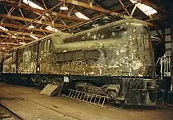 An unpainted, dirty-looking locomotive in a warehouse.