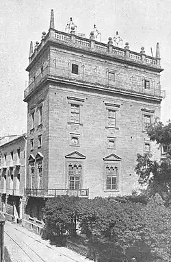 view of a building in black and white taken in 1911 with trees at the base of a rectilinear tower rising up five levels above the street