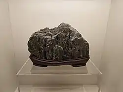 A craggy gray stone, cut to fit on a custom platform, displayed in an all-white museum diorama