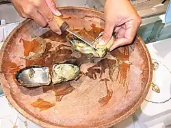 Photo of opened oyster in bowl with person using a knife to remove the pearl