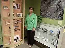 Dorothy Gunderson, of the Sunnyslope Historical Society and Museum, poses in front of the John C. Lincoln display in the historical building which once housed the "Peoples Drug Store".