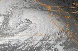 Satellite image of the Western United States, Western Canada, and the Pacific Ocean, with the states of the US shown in orange lines. The December 12, 1995 windstorm is visible as a dense formation of clouds to the left of the West Coast.