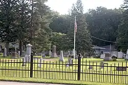 Cemetery grounds with US flag on flag pole in center of photo.