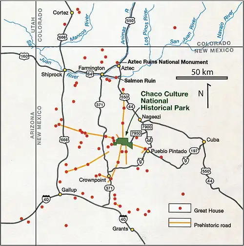 Large square map of northwestern New Mexico and neighboring parts of, clockwise from left, western Arizona, southeastern Utah, and southwestern Colorado. The map region has a green and blocky rectangular-crescent area at its center labeled "Chaco Culture National Historical Park". Radiating from the green region are seven segmented gold lines: "[p]rehistoric roads", each several dozen kilometers in length when measured according to the map scale factor. Roughly seventy red dots mark the location of "Great House[s]"; they are widely spread across the map, many of them far from the green area, near the extremes of the map, more than one hundred kilometers from the green area. Two proceed roughly south, one southwest, one northwest, one straight north, and the last to the southeast. Yellow dots mark the location of modern settlements: "Shiprock", "Cortez", "Farmington", and "Aztec" to the northwest and north; "Nageezi", "Cuba", and "Pueblo Pintado" to the northeast and east; "Grants", "Crownpoint", and "Gallup" to the south and southwest. They are connected by a network of gray lines marking various interstate and state highways. A fan of thin blue lines along the northern margins of the map depict the San Juan River and its communicants.